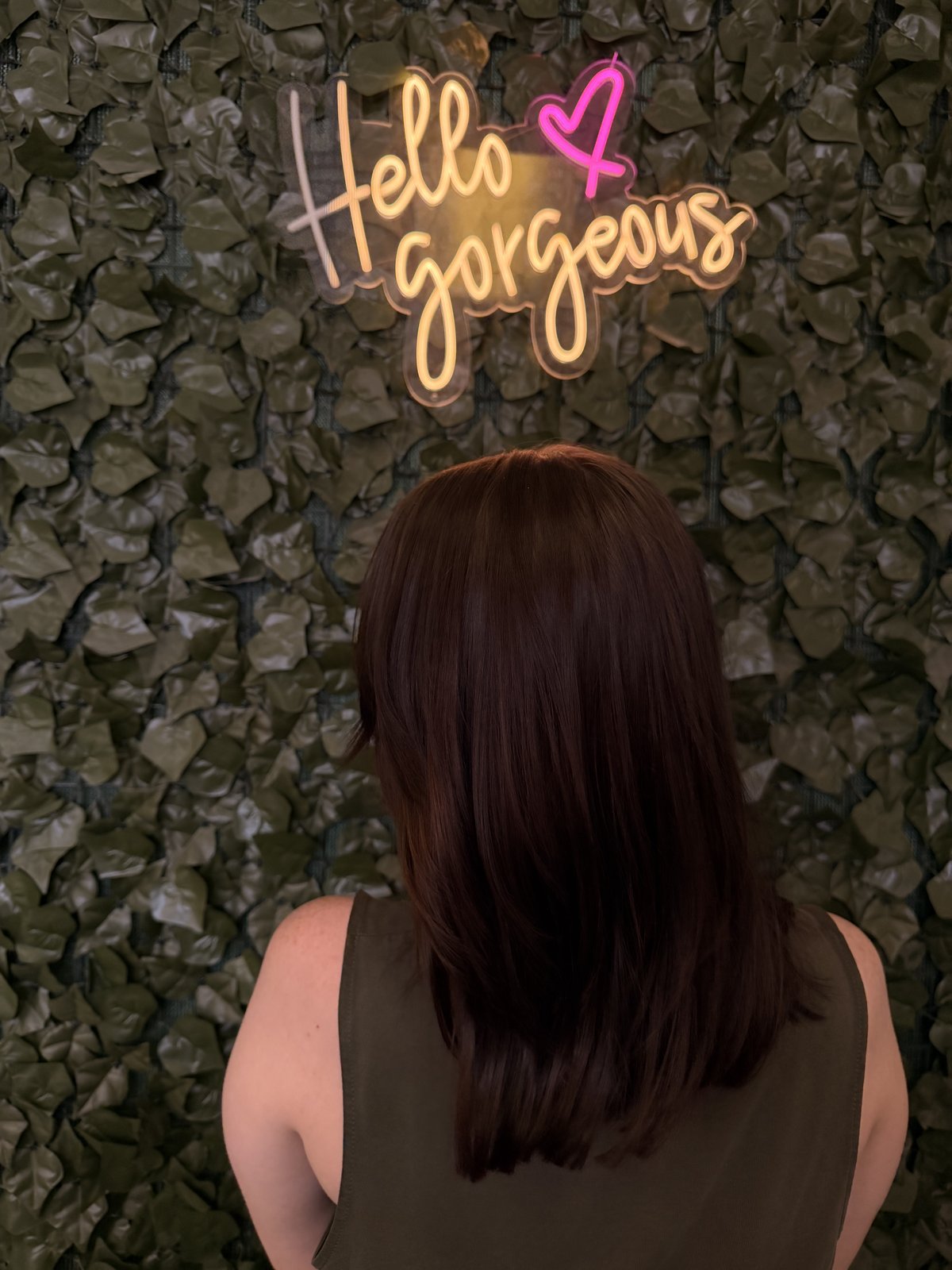 Auburn lob styled straight, signature green leaf wall behind.
